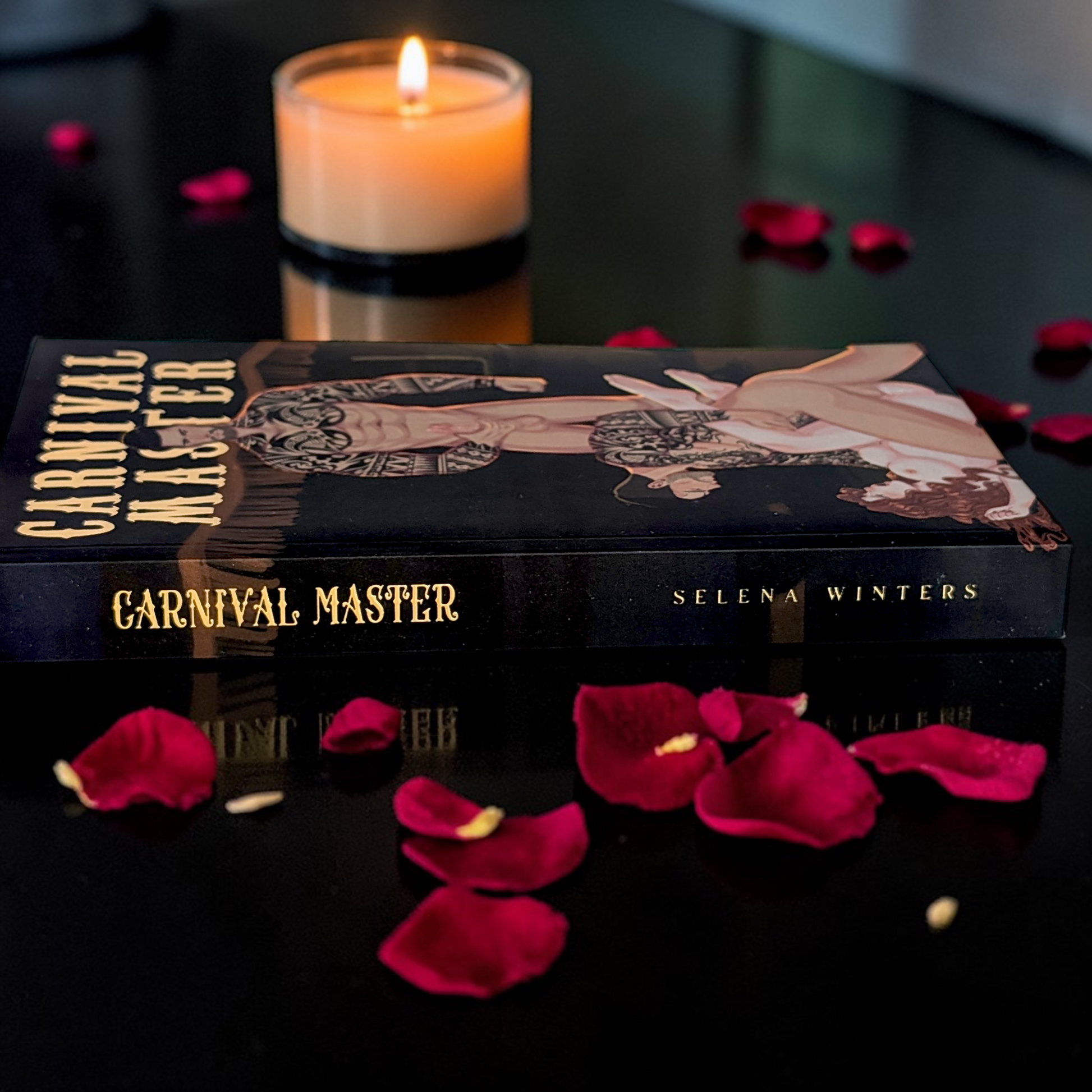 Book titled 'Carnival Master' by Selena Winters with a lit candle and red rose petals on a dark surface.